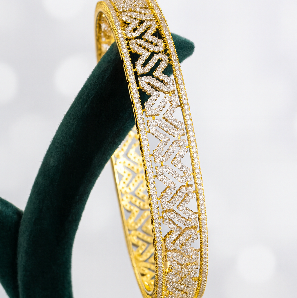 Gold bracelet with intricate patterns on a green stand against a light background