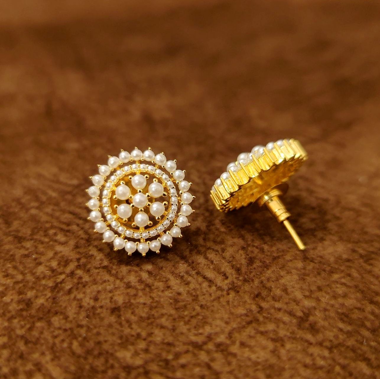 Gold and pearl earrings on a brown textured background
