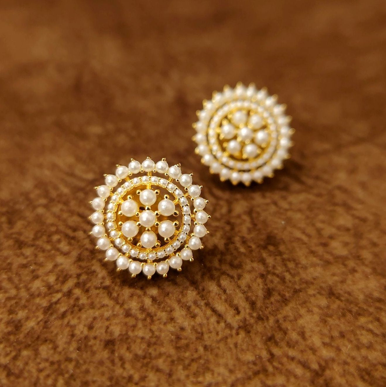Pair of gold and pearl earrings on a brown textured background