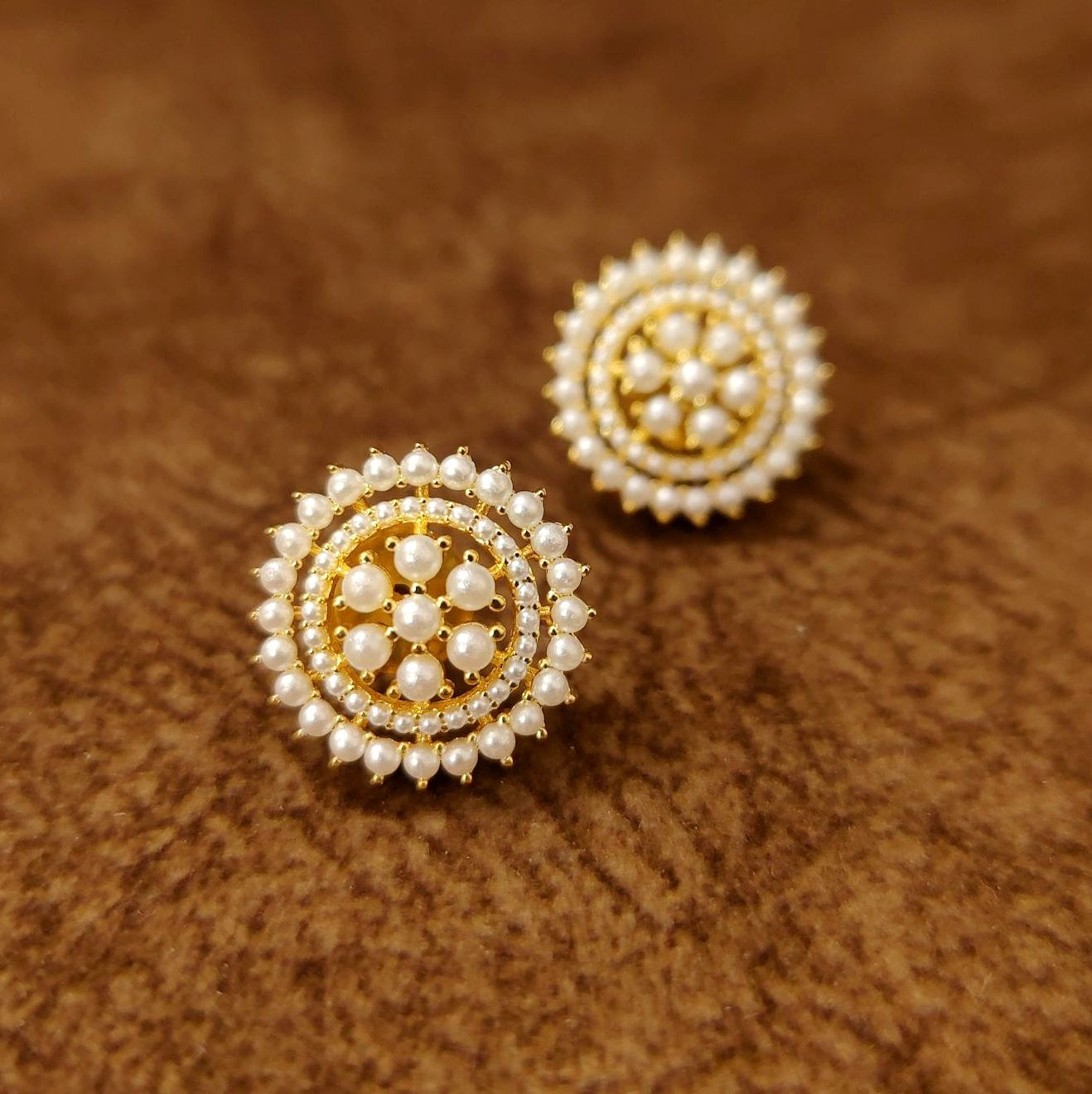 Pair of gold and pearl earrings on a brown textured background