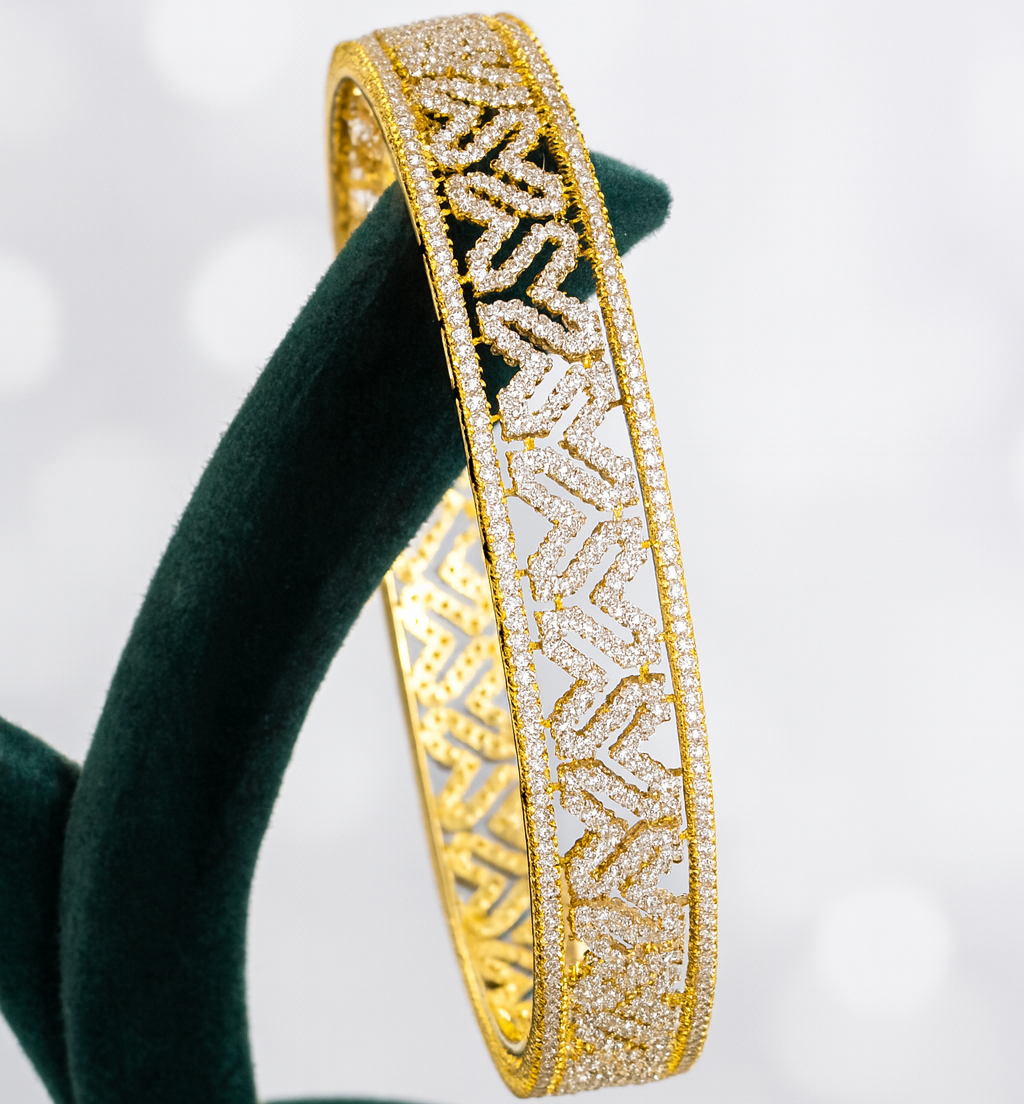 Gold bracelet with intricate patterns on a green stand against a light background