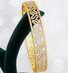 Gold bracelet with intricate patterns on a green stand against a light background